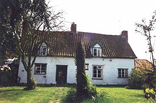 Front view of a medium sized building, painted white, and with a tiled roof which contains two dormer windows.