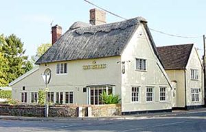 A cream coloured thatched two story building on the corner of one part of the crossroads. Gold lettered sign on side “Six Bells”.