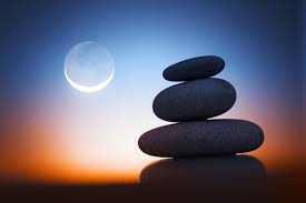 stacked pebbles against a blurred blue and orange sky and the moon low in the sky