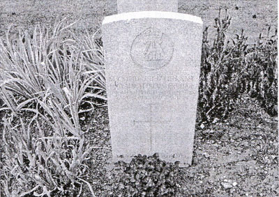 A black and white photograph of Oswald's grave at St Sever showing a gravestone surrounded by plants. There are inscriptions on the gravestone but they are not very clear to read.
