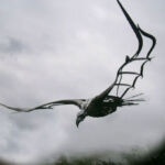 'Bird' by Peter Rudderham Cast iron bird of prey with large wing span and eagle like head and beak, wings spread in full flight against a grey cloudy sky.