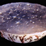 Cast Glass by Mandy Jaggard A piece of case glass in the shape of a bowl which is white, cream with brownish red markings that give the impression of natural veining. The top of the object has a surface that looks like the sun glinting on the waves of the sea making the object look like a bowl full of water in motion.