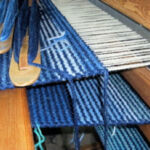 Woven rug in progress, Mary-Jane Toulson An image of wool in various shades of blue through to a light cream in the process of being woven on a loom into a rug.